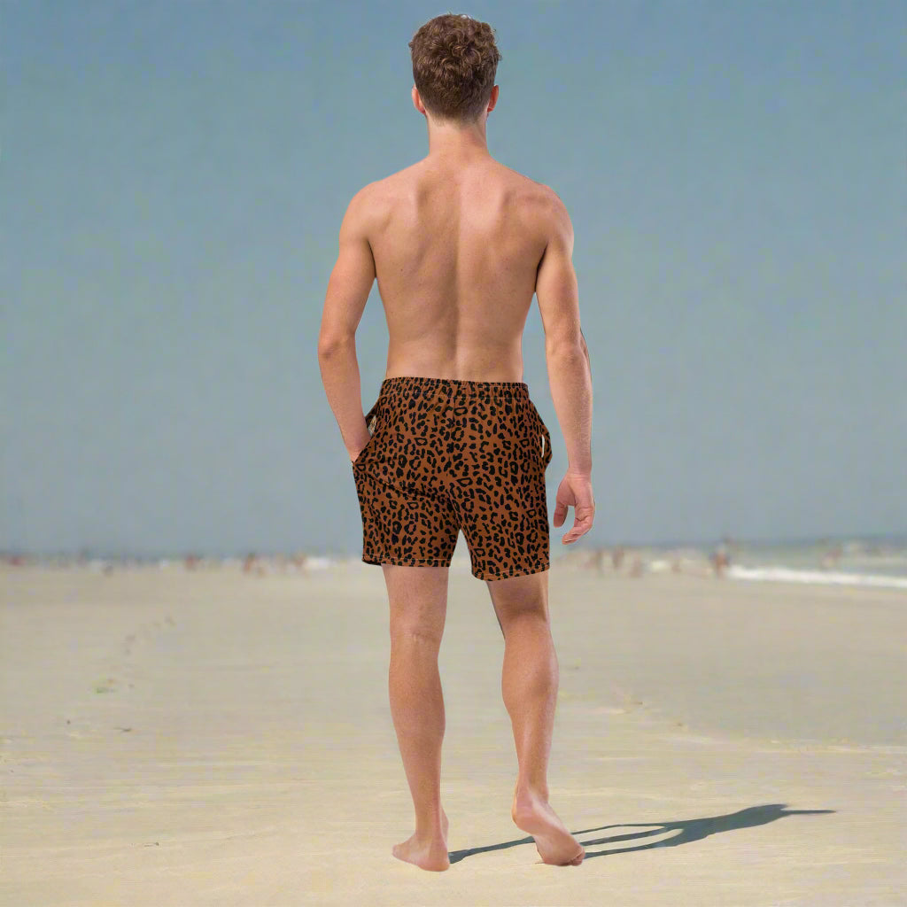 Man walking on the beach with cheetah print bathing suit on in dark brown and warm chocolate colors.