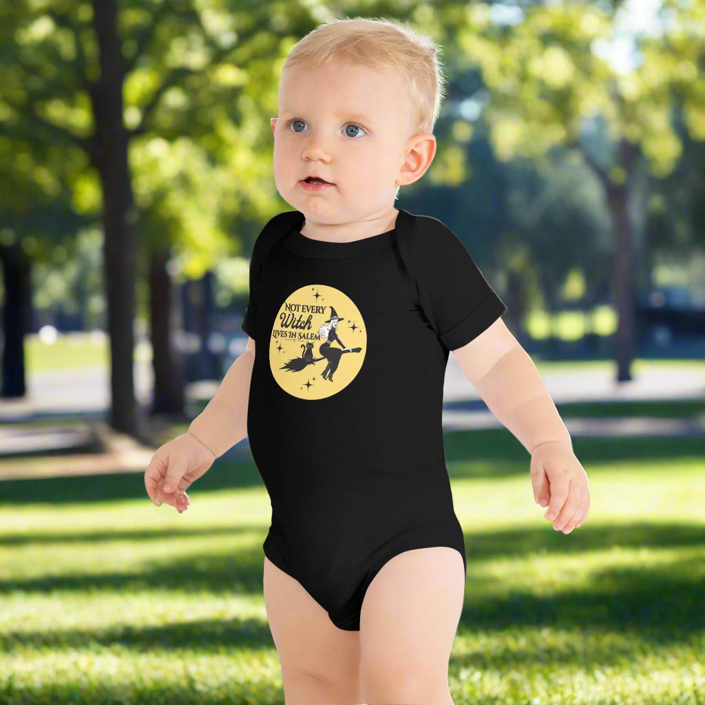 baby in a short sleeve onesie that has a yellow moon, pretty witch and black cat riding on a broom, the words "Not Every Witch Lives in Salem" on it.