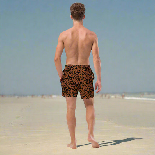 Man walking on the beach with cheetah print bathing suit on in dark brown and warm chocolate colors.